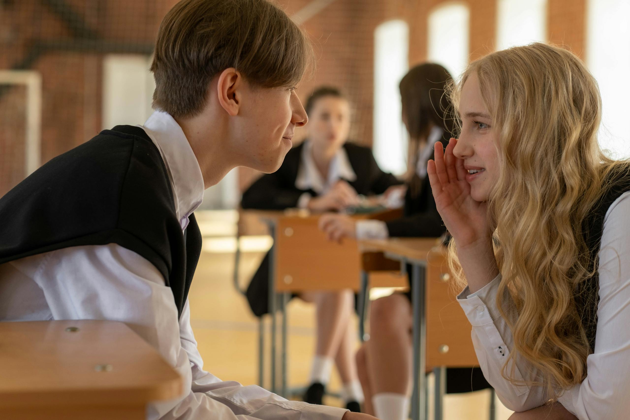 Two students whisper and converse in a school classroom, adding a lively atmosphere. Photo by cottonbro studio